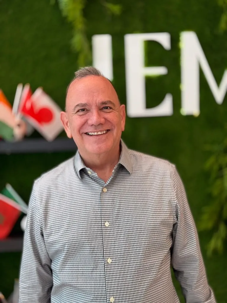 Portrait of Francisco “Kiko” Angulo smiling in front of a wall of international flags