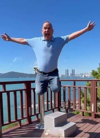 Kiko jumping with arms outstretched on a seaside overlook