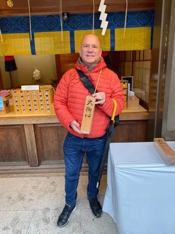 Kiko in a red jacket holding a wooden plaque inside a temple