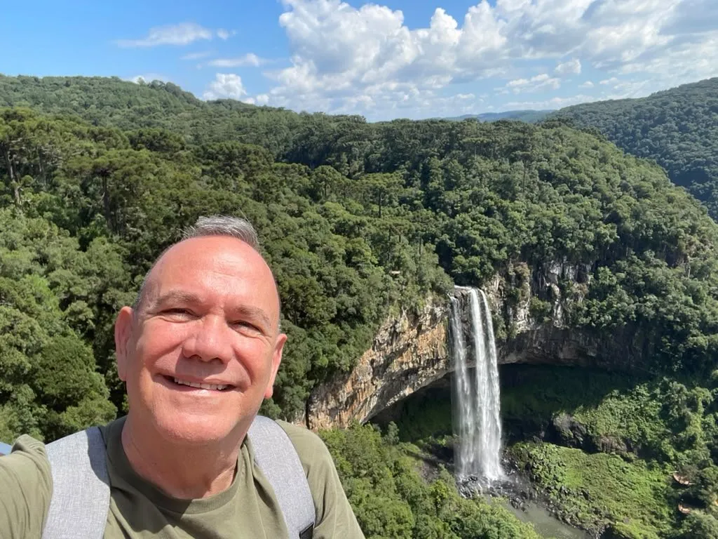 Kiko smiling in front of a waterfall in a forested canyon